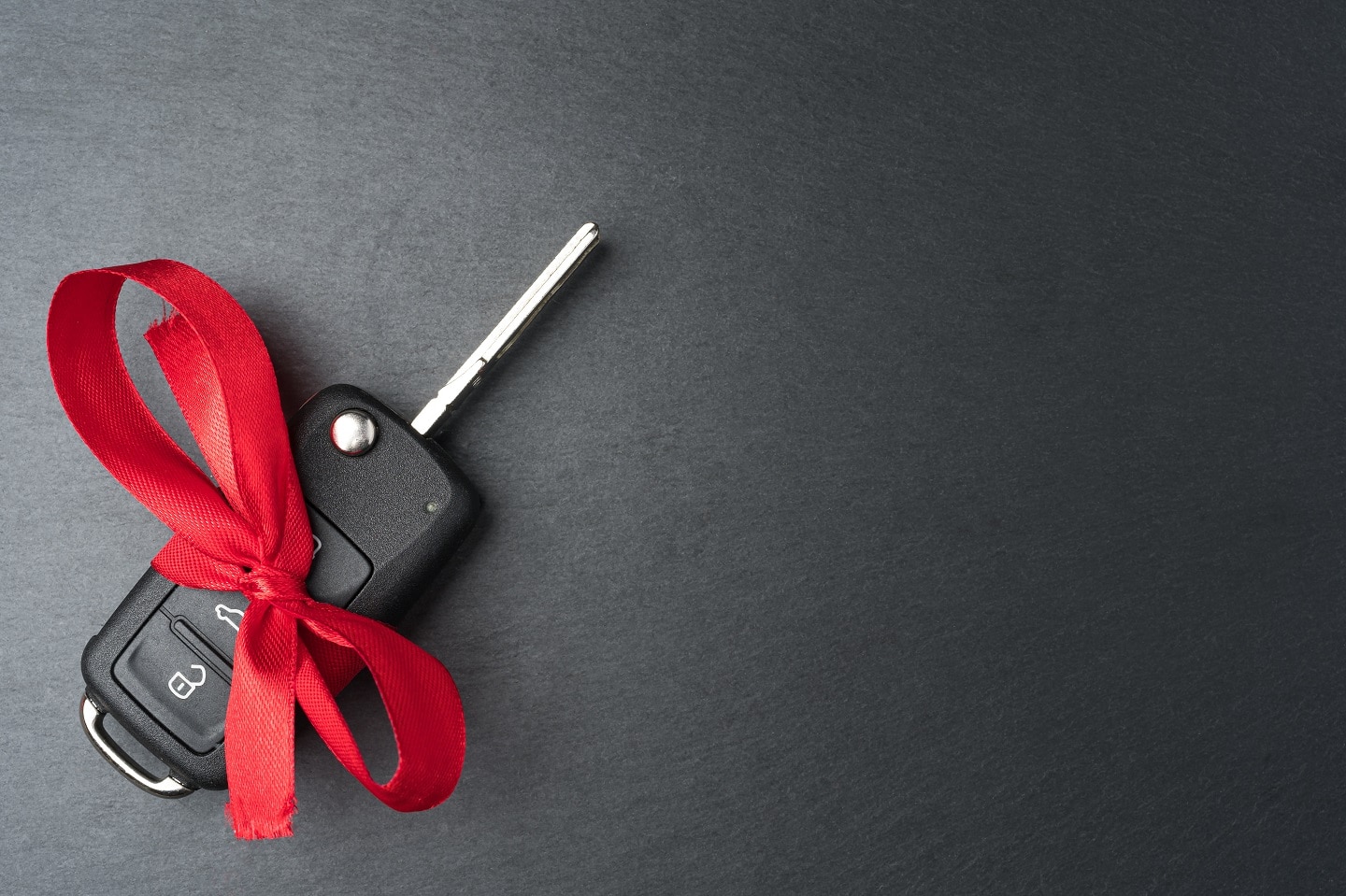 LEMAC Canada Car key with red bow on dark black slate plate background. Christmas or Valentine's Day gift or present abstract concept. Copy space on the right. Flat lay top view.